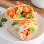 A Sweet Potato Breakfast Burritos cut in half and the halves are stacked on top of each other on a plate.