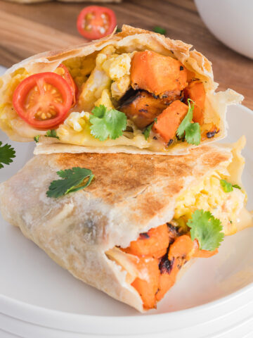 A Sweet Potato Breakfast Burritos cut in half and the halves are stacked on top of each other on a plate.