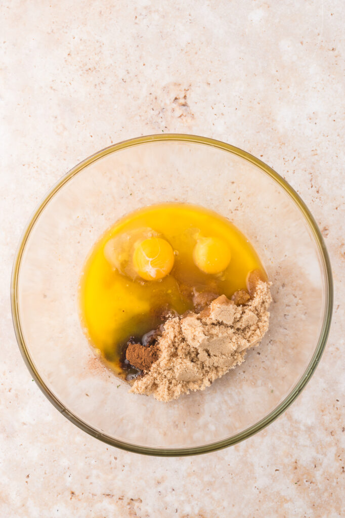 A glass bowl of melted butter, brown sugar, eggs, vanilla extract and ground cinnamon.