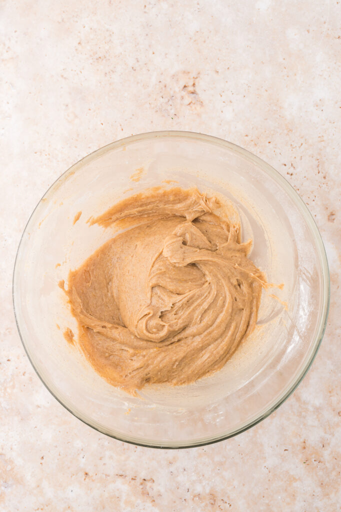 A glass bowl of melted butter, brown sugar, eggs, vanilla extract and ground cinnamon mixed together.