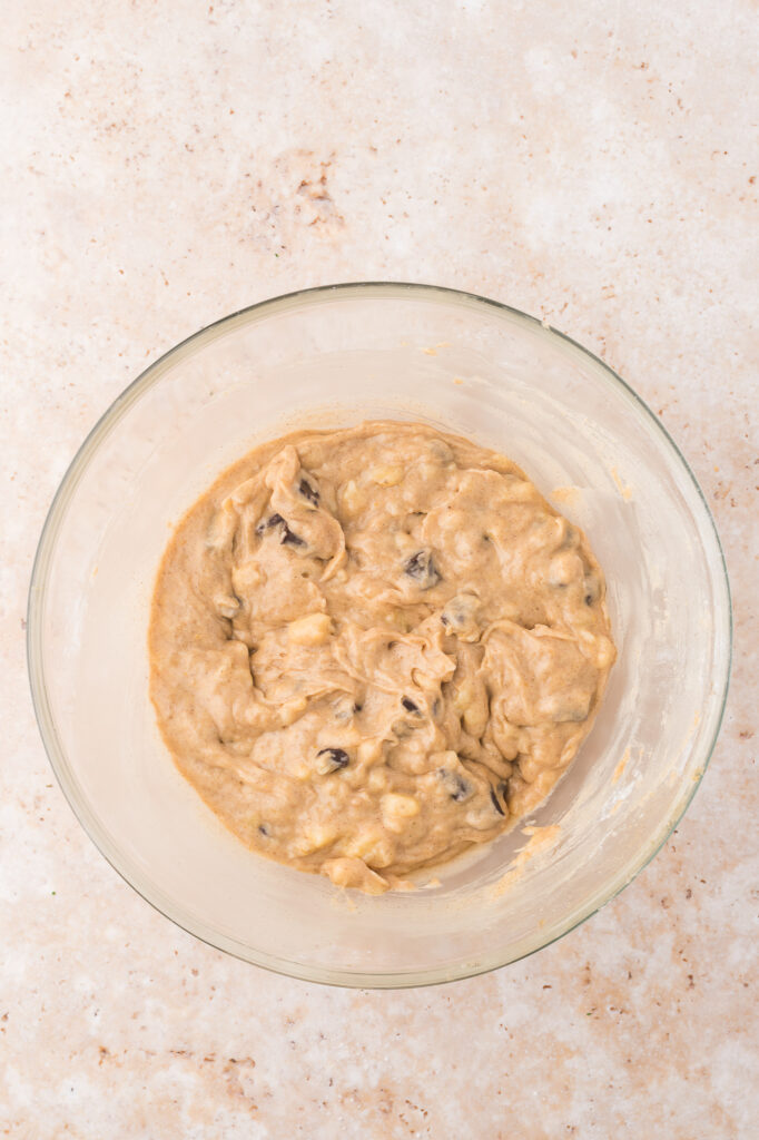 A glass bowl of the wet and dry ingredients mixed together with the banana added in.