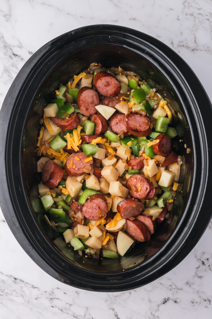 All the ingredients plus the sauce in the slow cooker for Slow Cooker Sausage Potato Casserole.