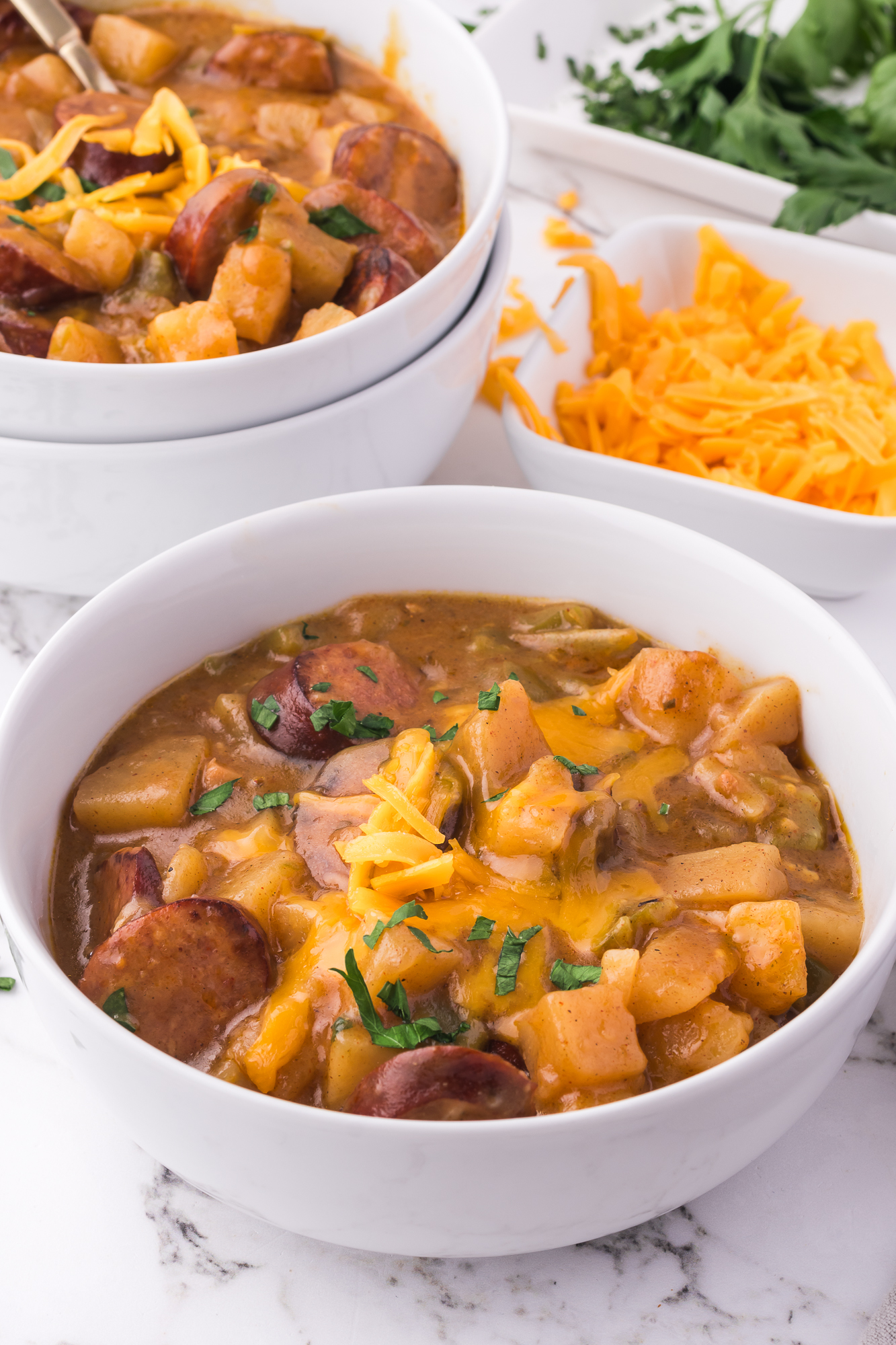 Two white bowls of Slow Cooker Sausage Potato Casserole topped with shredded cheese.