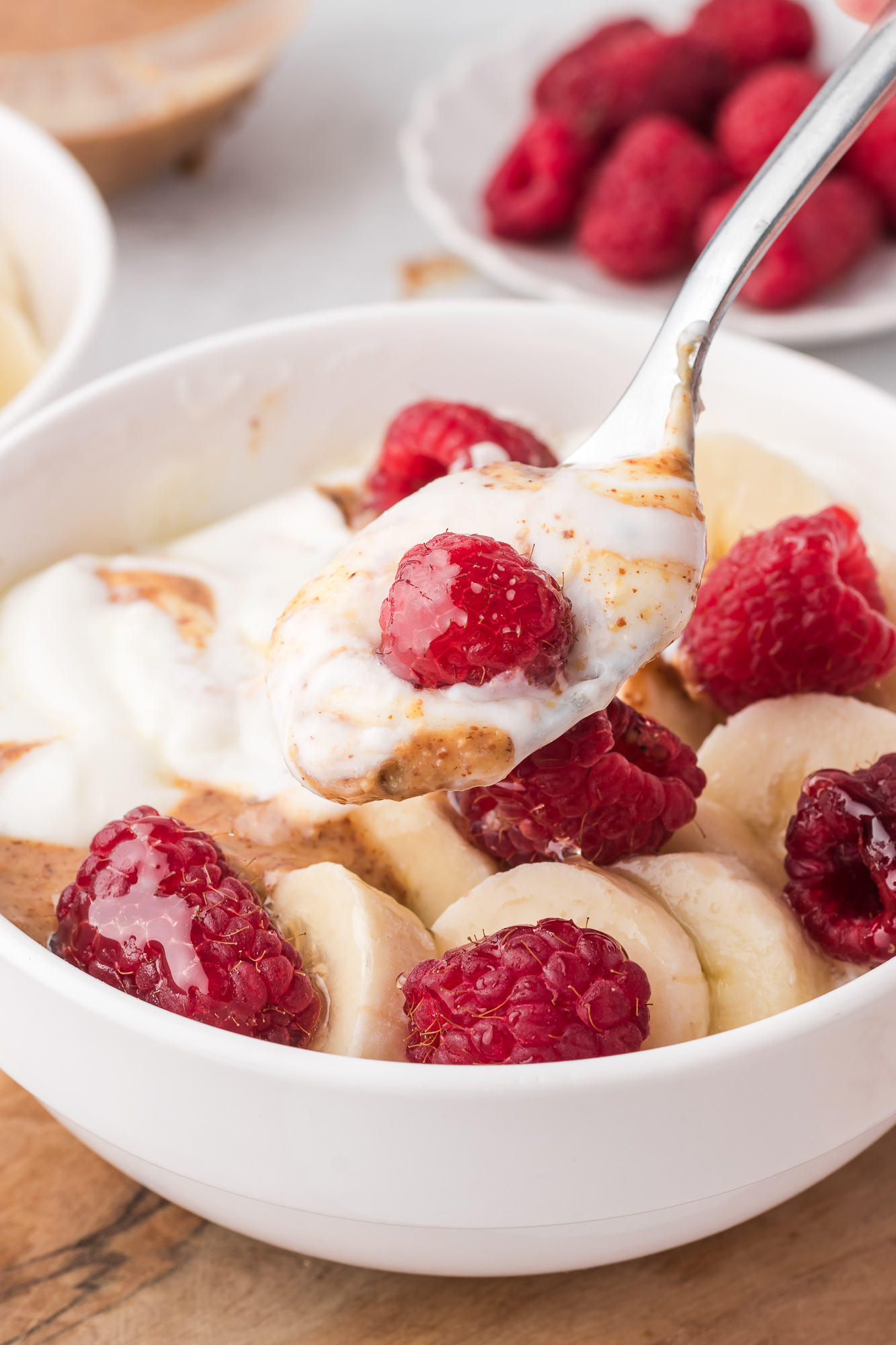 A close-up of a spoon holding a spoonful of Two Whipped Cottage Cheese Bowls topped with bananas, raspberries, and almond butter.