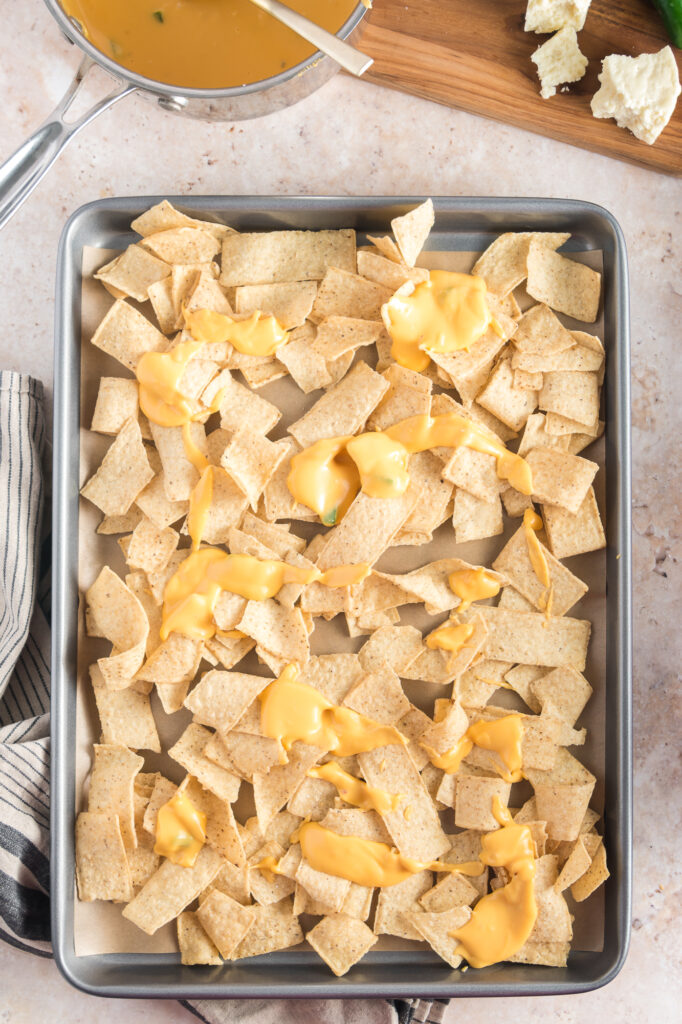 A sheet pan of nachos drizzled with cheese for Sheet Pan Nachos.