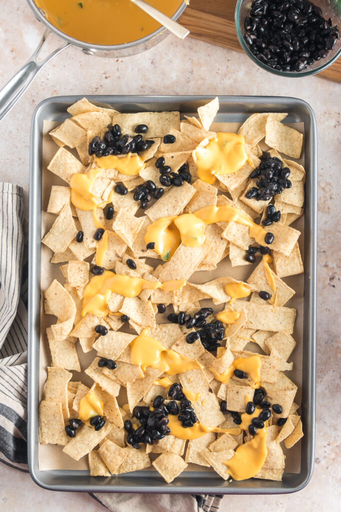 A sheet pan of nacho strips, cheese, and black beans for Sheet Pan Nachos.