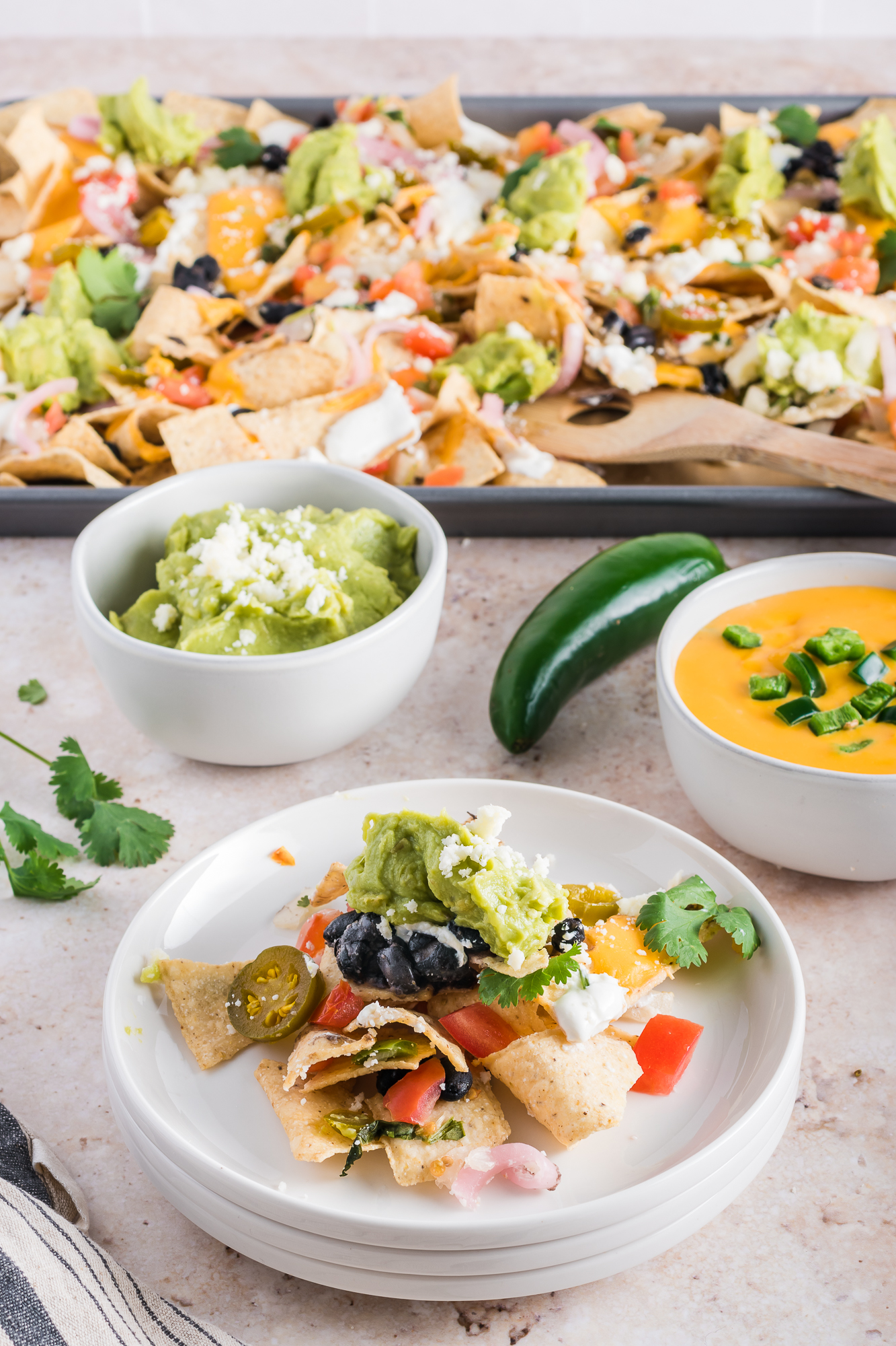 A plate of Sheet Pan Nachos with guacamole and queso and a tray of Sheet Pan Nachos in the background.