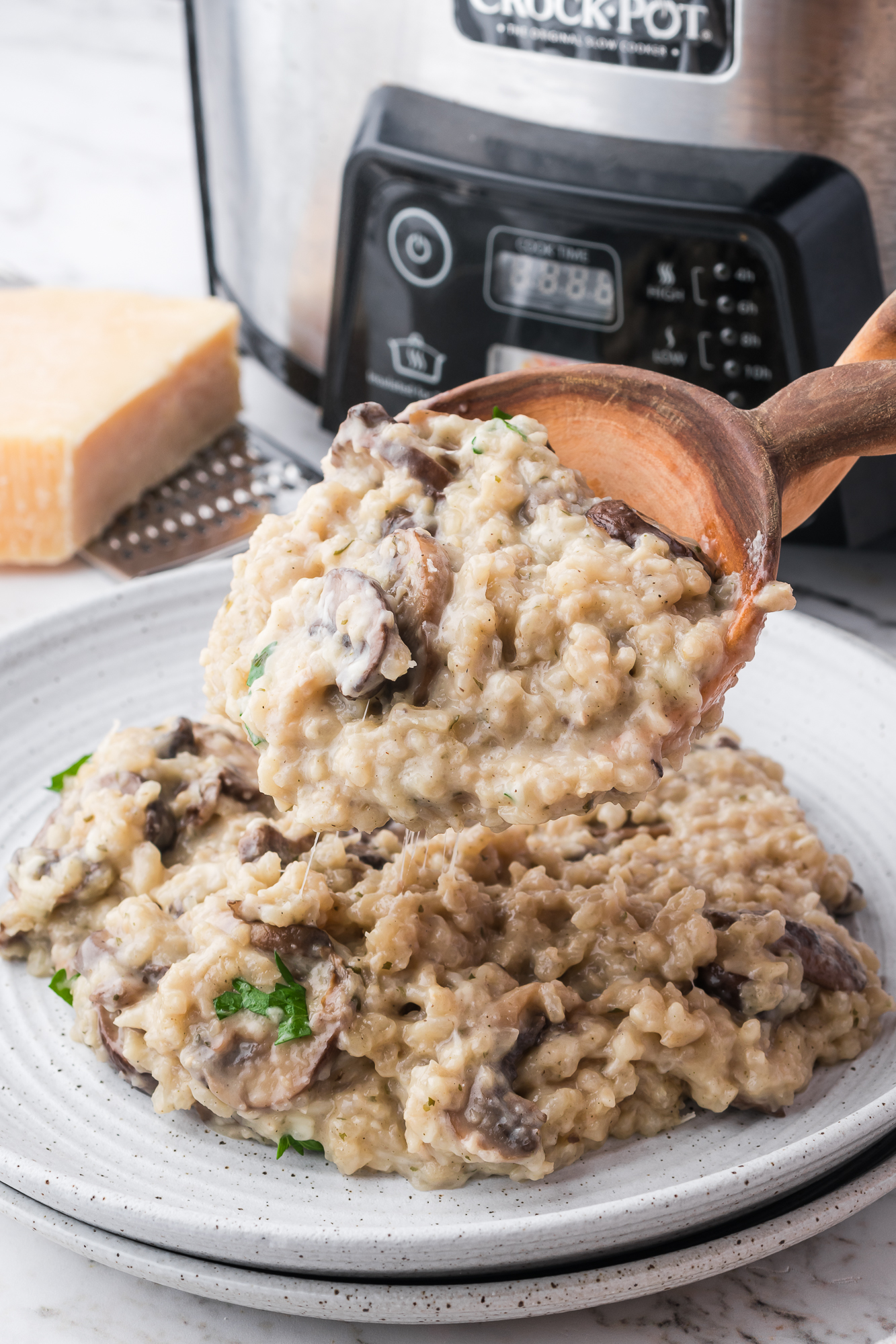 A wooden spoon scoops Slow Cooker Mushroom Risotto onto a plate.