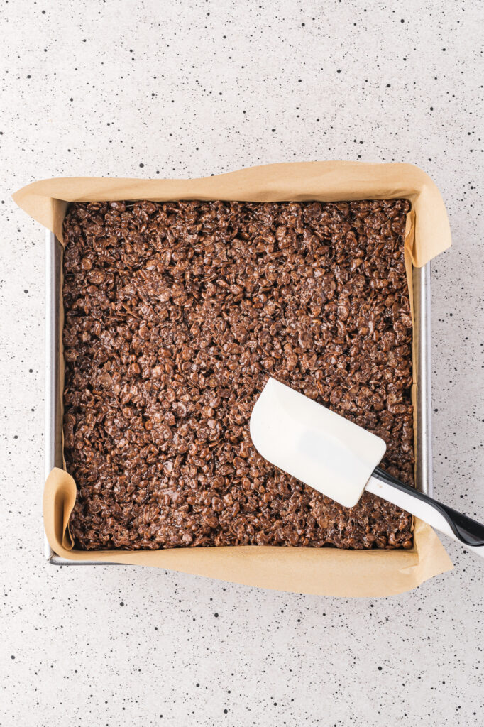 A parchment-lined brownie pan filled with the Spooky Cocoa Pebbles Treats mixture.