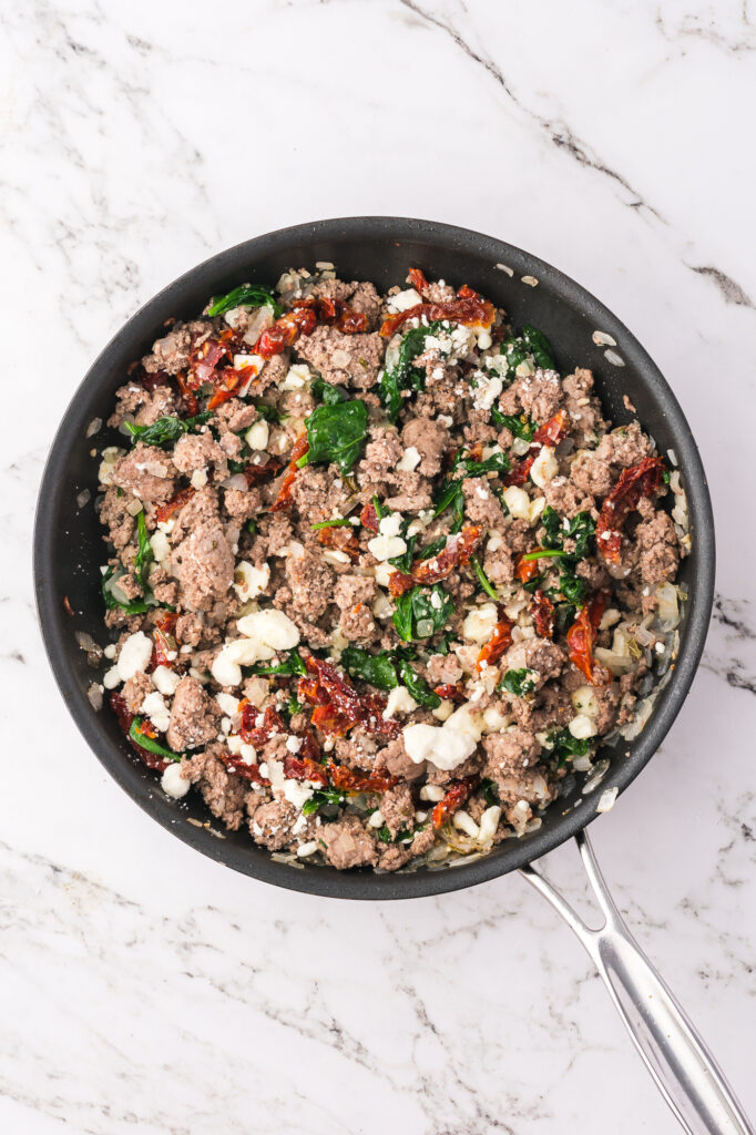 A skillet with a turkey, vegetable, and cheese mixture.