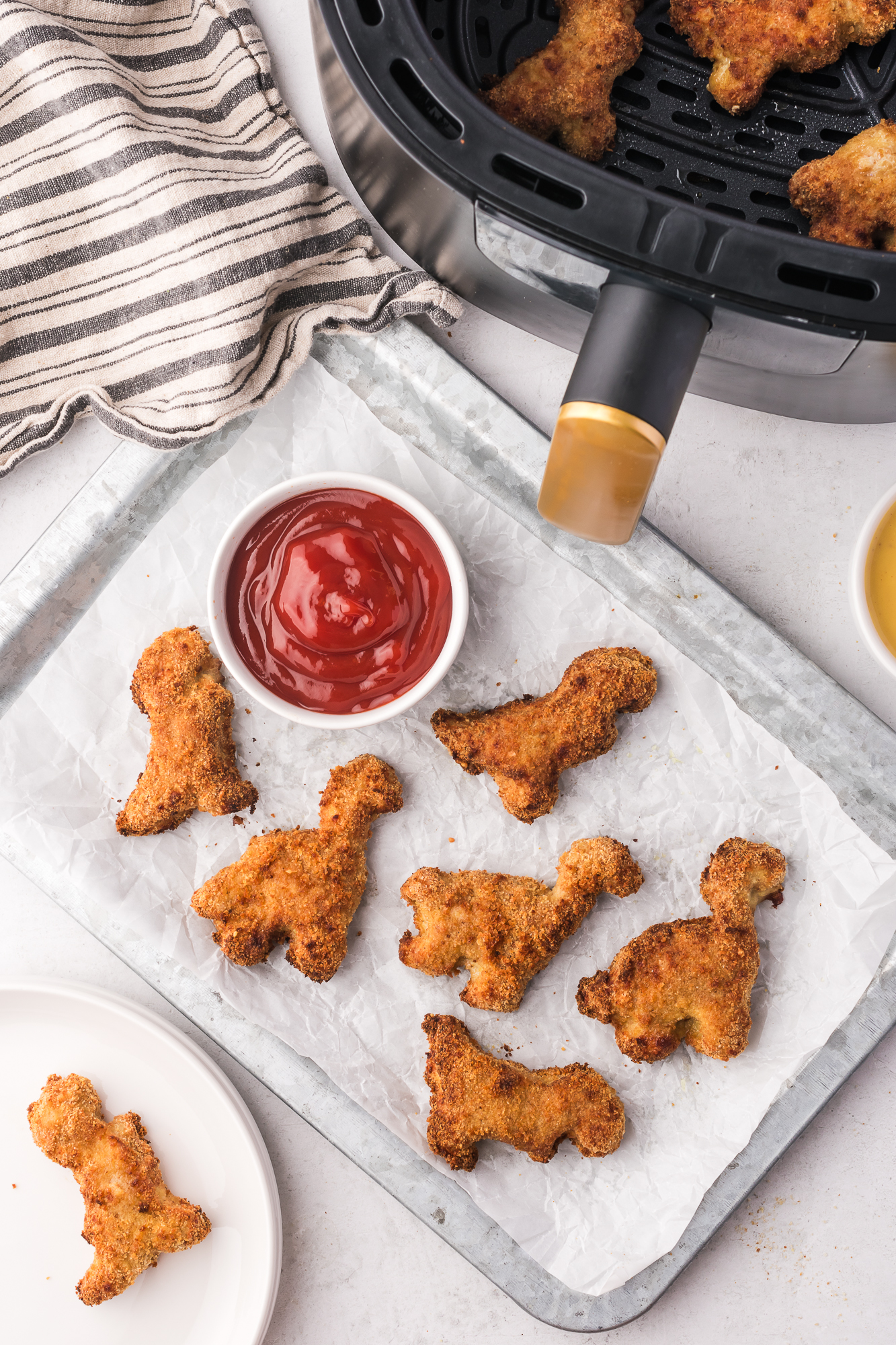 A parchment-lined tray of Air Fryer Dino Chicken Nuggets with a small bowl of ketchup.