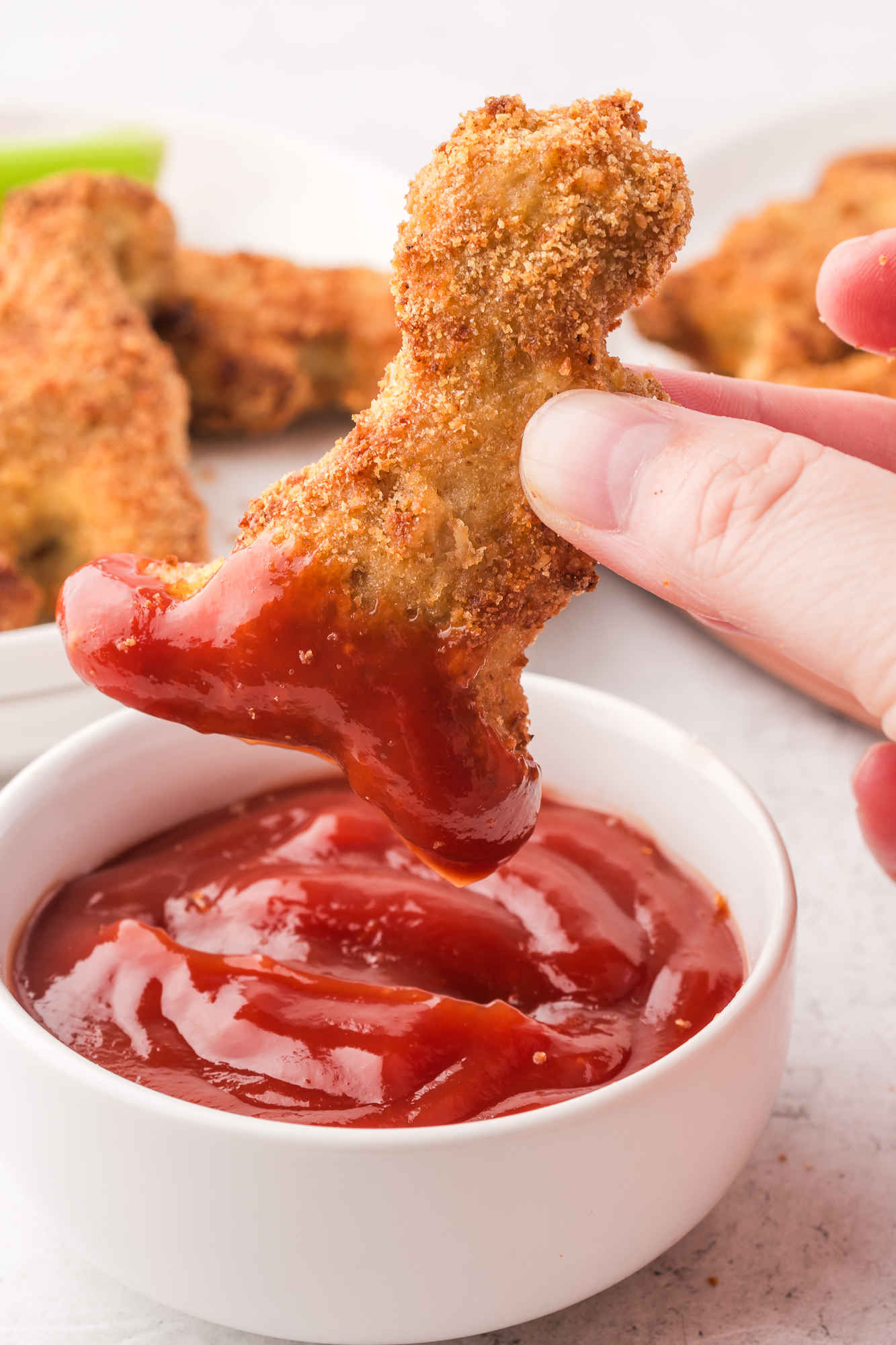 A Air Fryer Dino Chicken Nugget being dipped into ketchup.