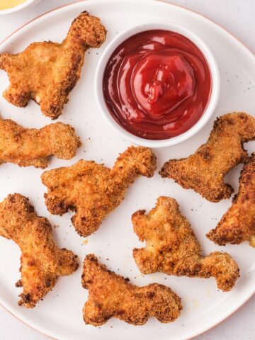 A plate of Air Fryer Dino Chicken Nuggets with a small bowl of ketchup.