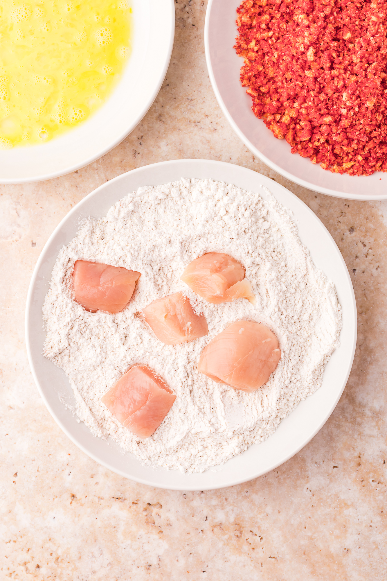 Raw pieces of chicken being covered in flour.