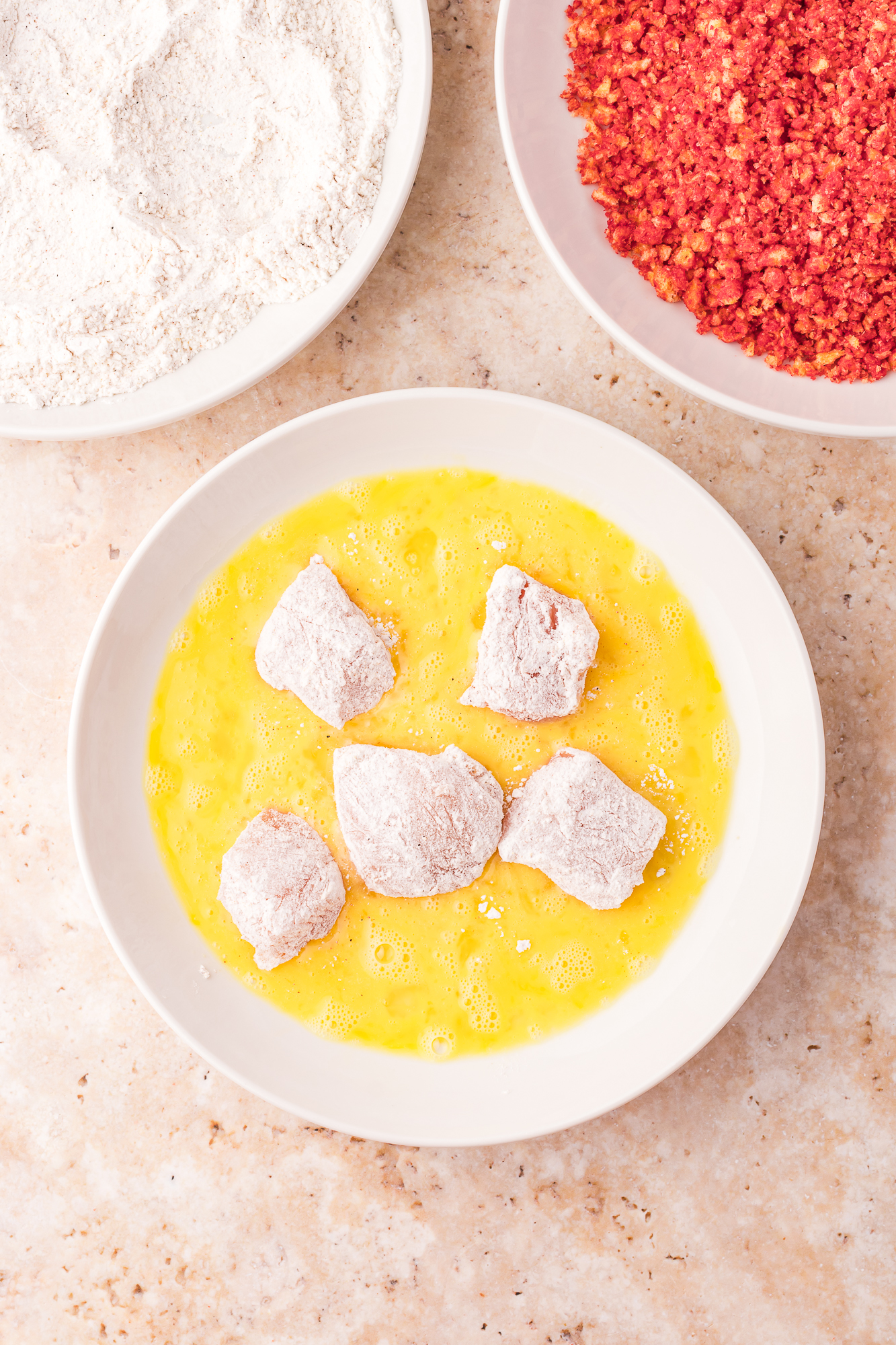 Flour-coated pieces of chicken being dipped in egg.