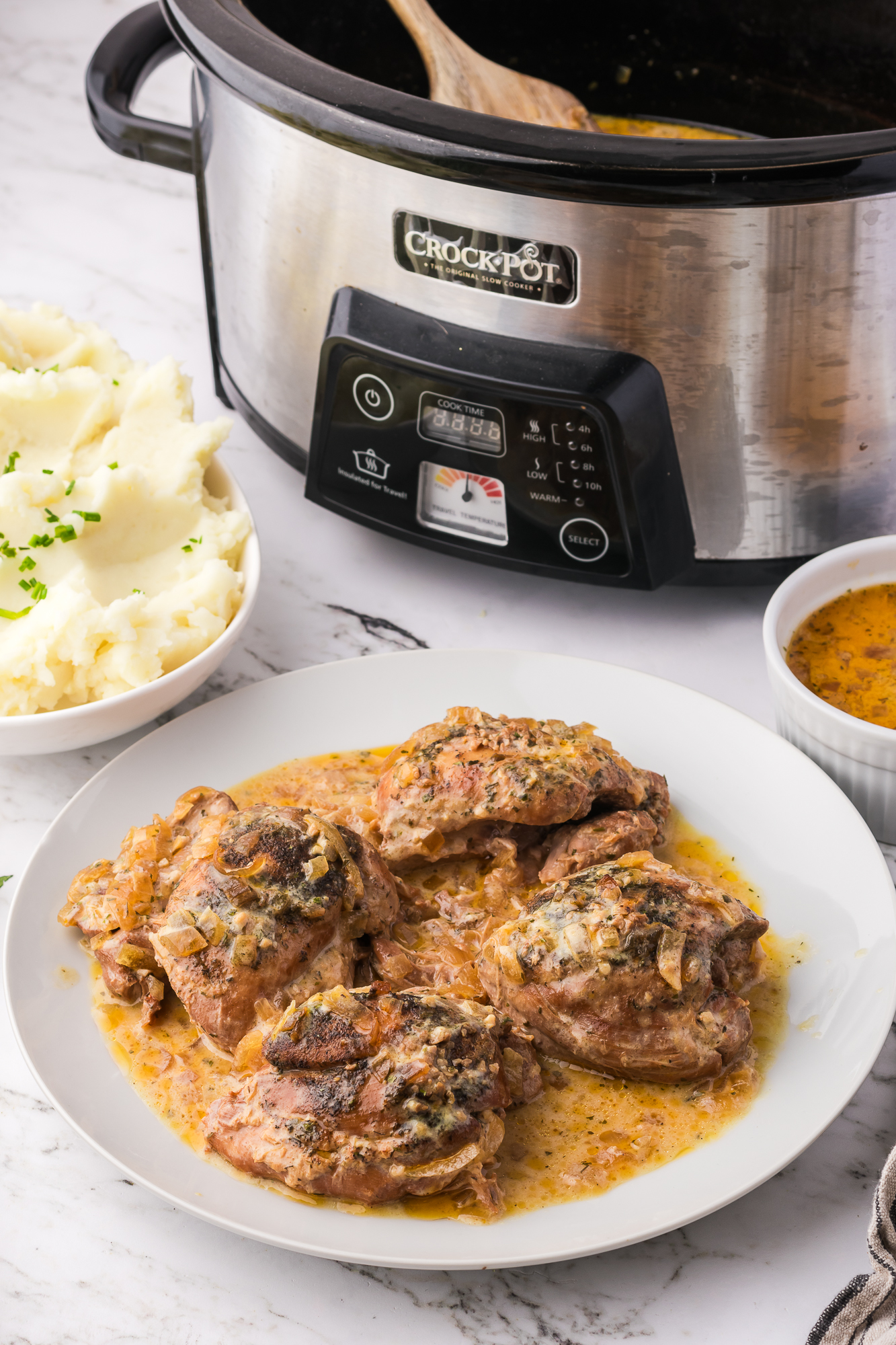 A white plate of four Slow Cooker Ranch Chicken breasts in front of slow cooker.