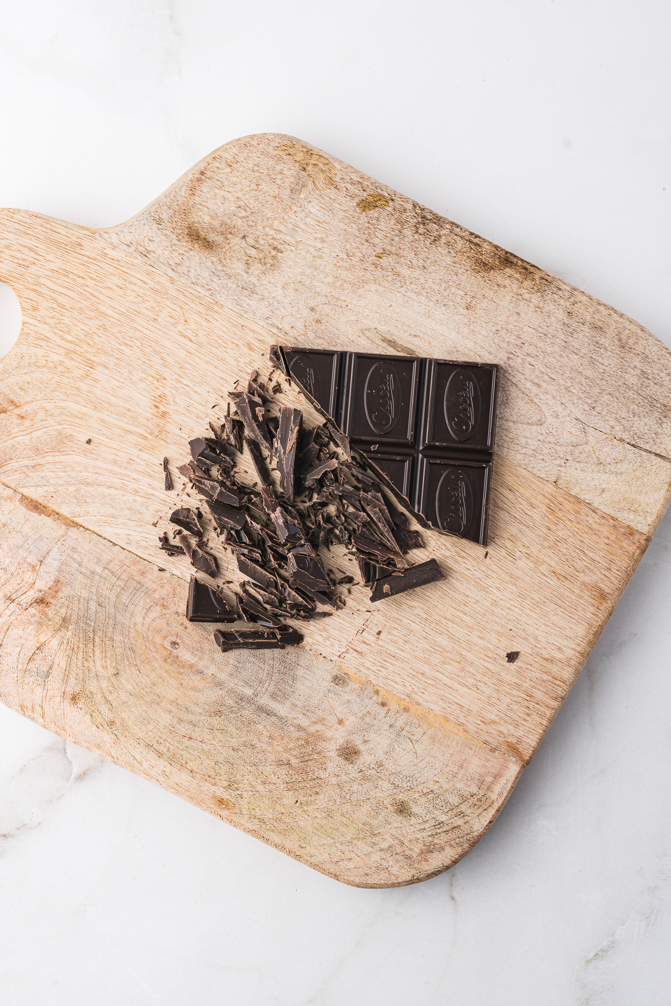 Some chocolate being chopped on a wooden cutting board.