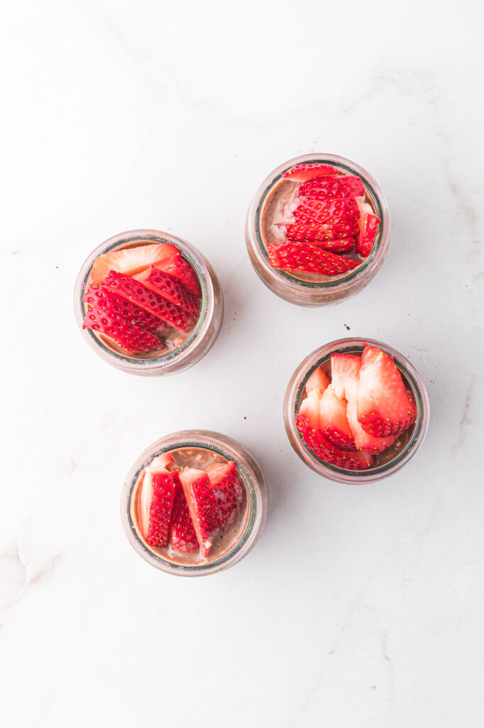 The four glass jars of Nutella Overnight Oats topped with sliced strawberries.