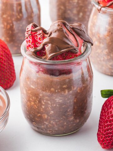 Nutella Overnight Oats in small glass jars surrounded by strawberries.