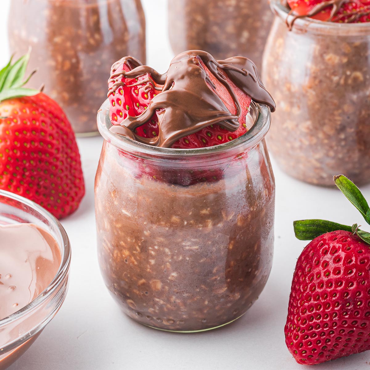 Nutella Overnight Oats in small glass jars surrounded by strawberries.