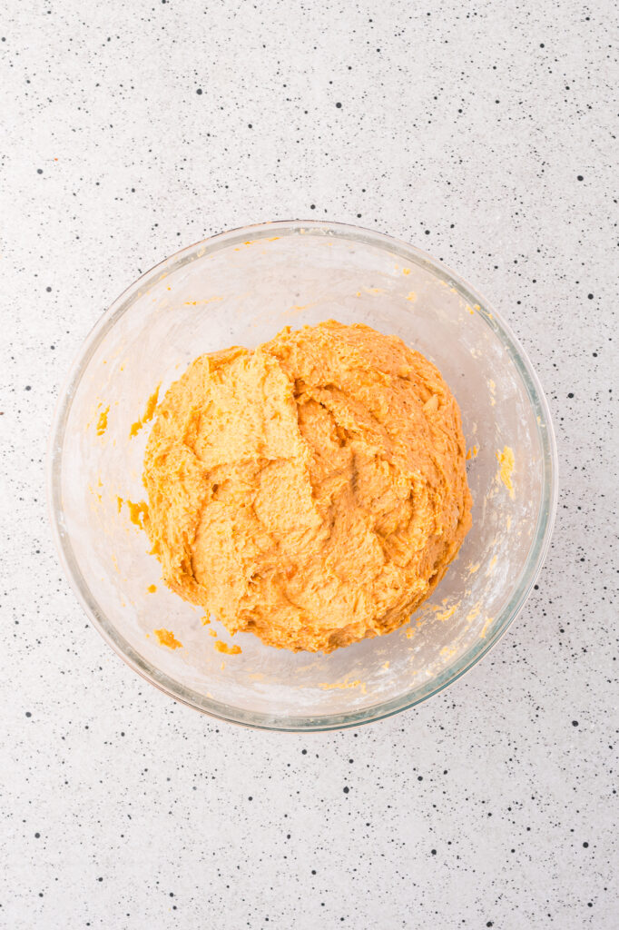 A glass bowl of the prepared sweet potato mixture with flour added.