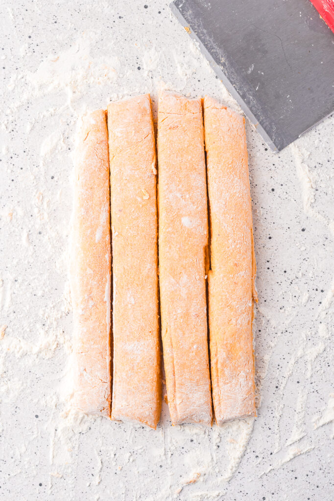 The rolled out gnocchi dough cut into four long strips.