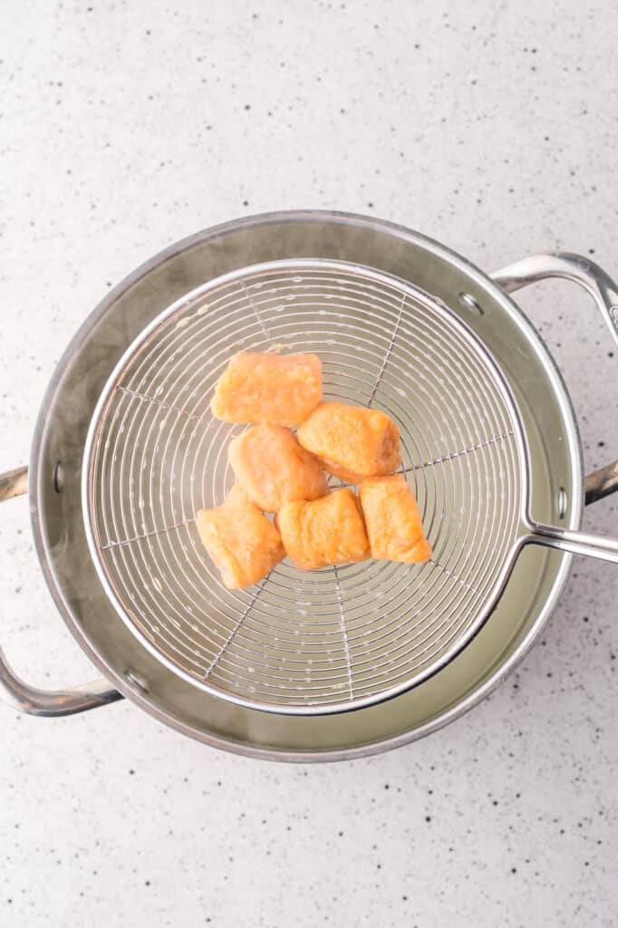 Pieces of sweet potato gnocchi in a sieve coming out of a pot of boiling water.