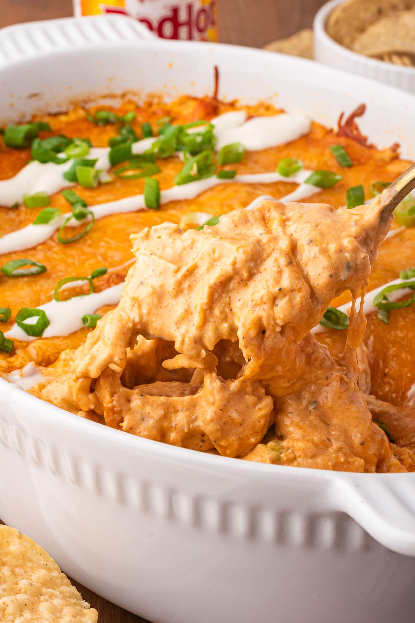 A close up of a spoon serving Buffalo Chicken Dip with Frank's Buffalo Sauce from the casserole dish.