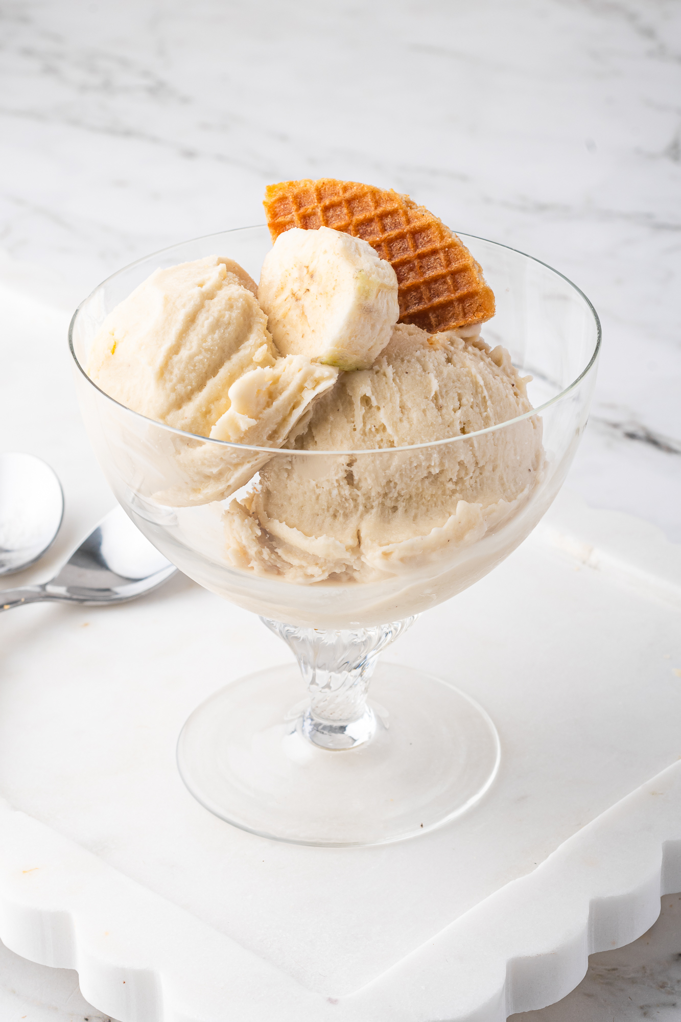 A glass bowl of Ninja Creami Banana Ice Cream with a slice of banana and a stroopwafel piece.