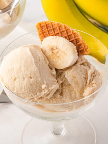 A glass bowl of Ninja Creami Banana Ice Cream with a slice of banana and a waffle cone piece.