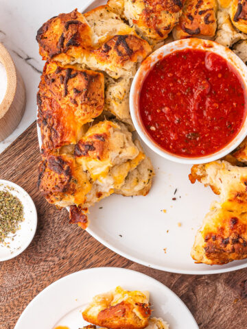 A serving plate of Cheesy Pull-Apart Bread with marinara sauce next to a plate with a smaller serving of it.