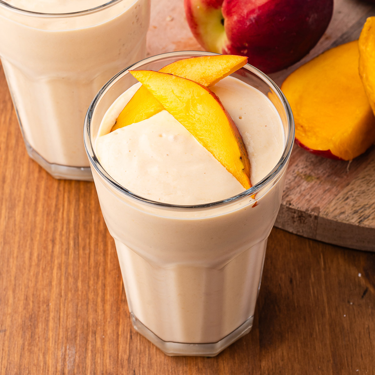 Two glasses of Cottage Cheese Fruit Smoothie with sliced mango on top.
