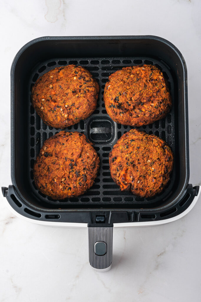Four baked patties of sweet potato and black bean mixture in the basket of an air fryer