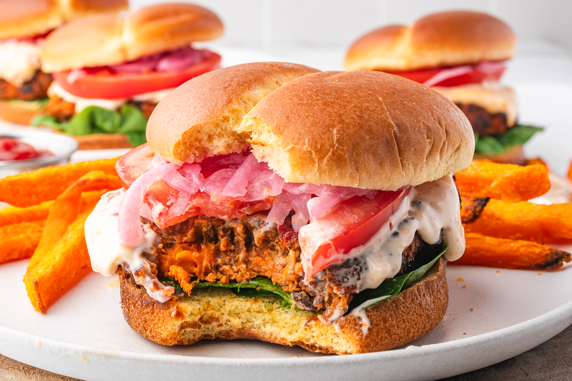 A close-up of a bite taken out of An Air Fryer Sweet Potato and Black Bean Burger with Sun-dried Tomato Aioli on a hamburger bun