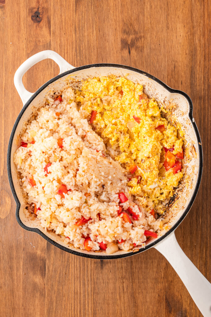A skillet that is half rice mixture and half cooked scrambled eggs