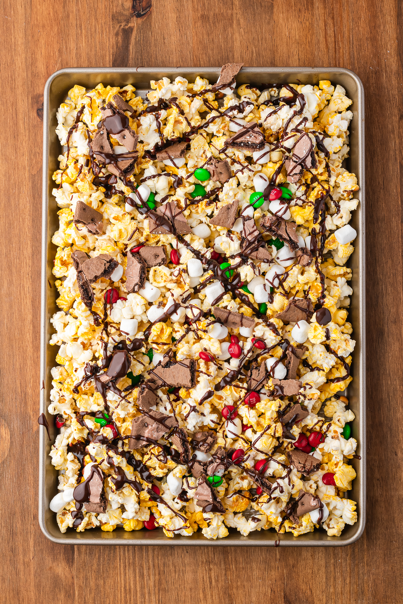 A cookie sheet of popped popcorn tossed with M&M's, marshmallows, and pieces of Pop Tarts drizzled with chocolate sauce