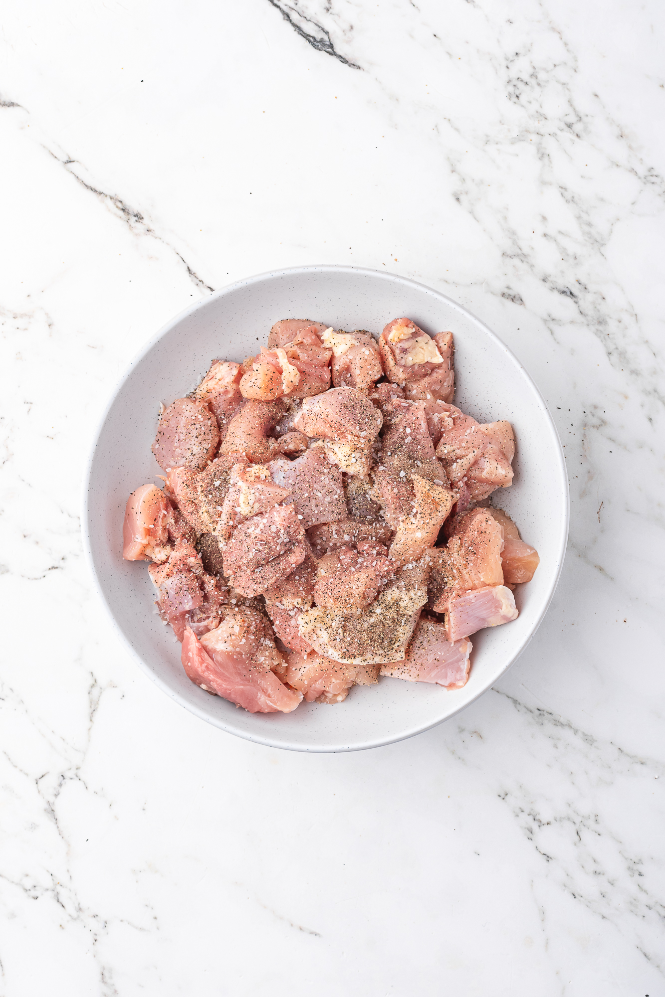 A bowl of seasoned chicken thighs cut into large pieces