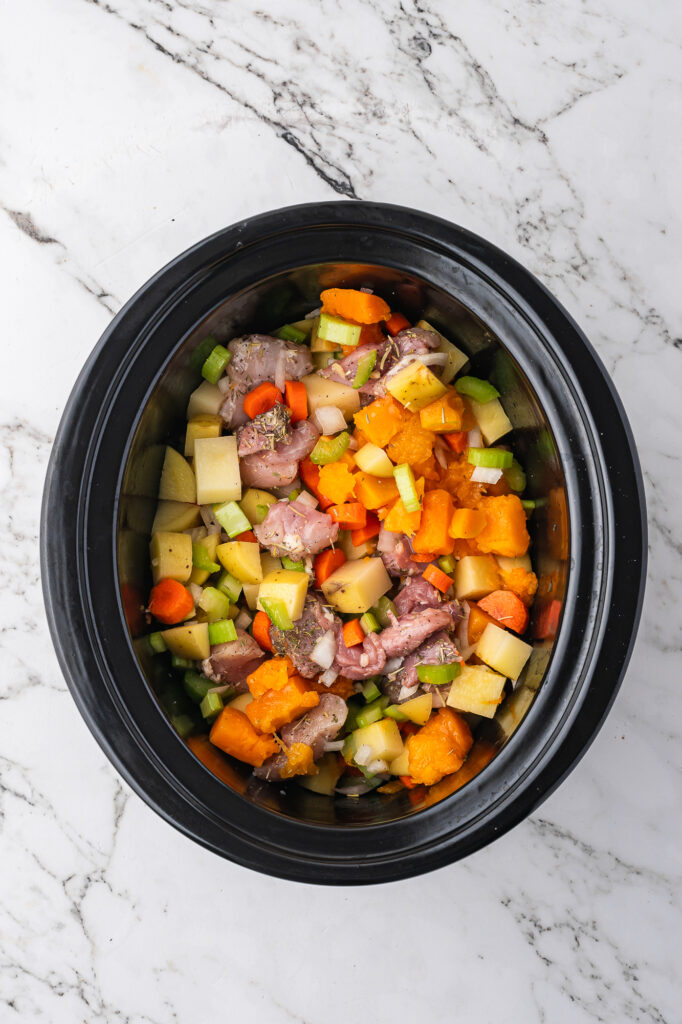 A slow cooker full of all the ingredients for Slow Cooker Hearty Chicken Stew before the broth