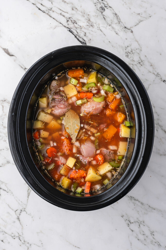 A slow cooker full of all the ingredients for Slow Cooker Hearty Chicken Stew with the broth