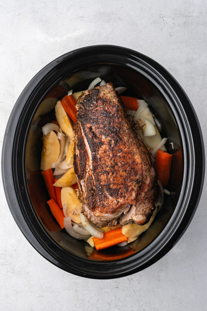 The browned pork on top of the veggies in the slow cooker
