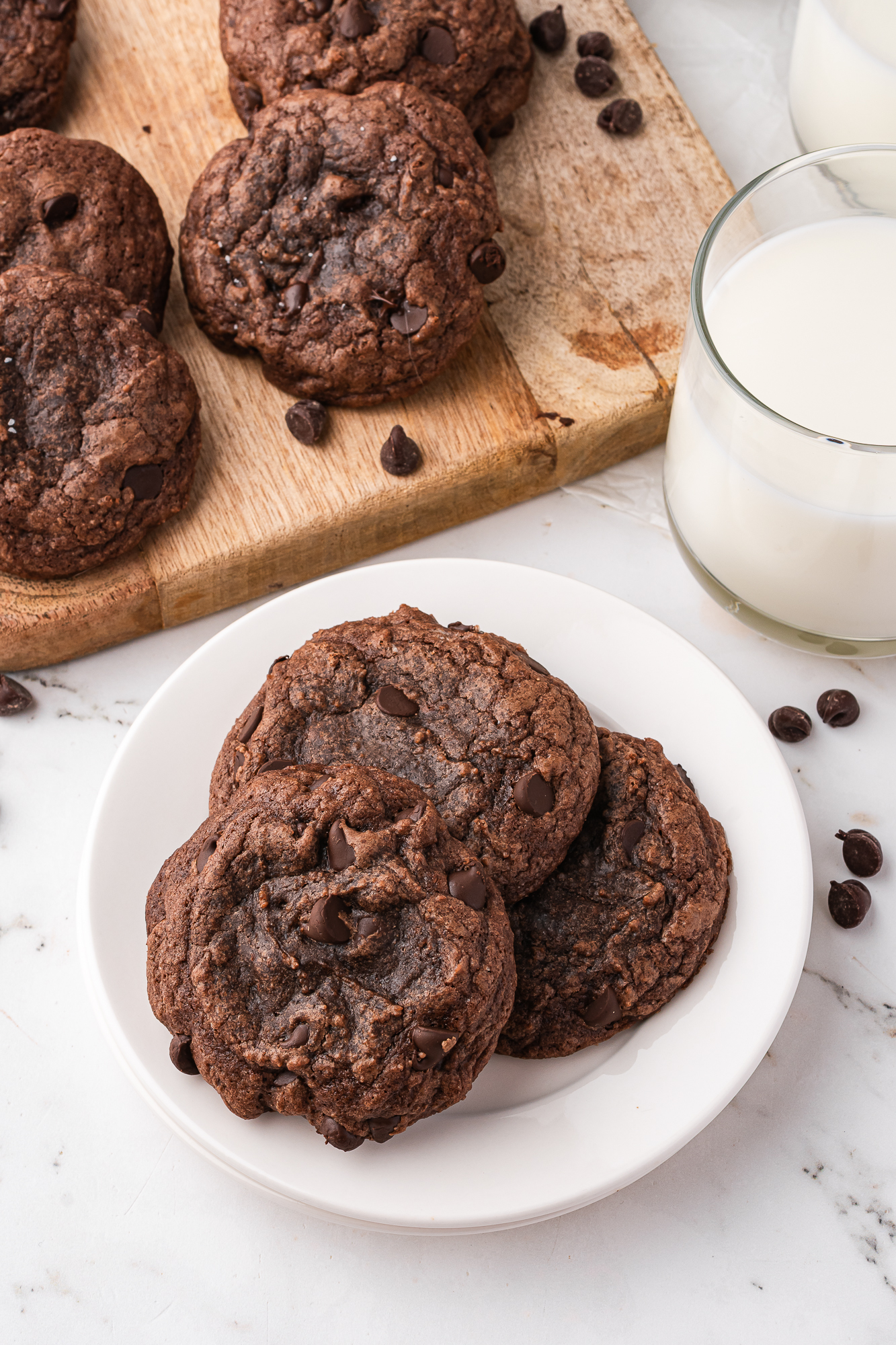 A white plate with 3 Easy Brownie Mix Cookies next to a glass of milk and a wooden board of extra cookies