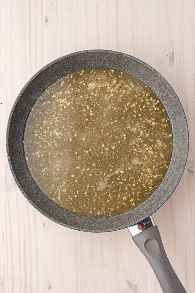 A skillet with a layer of oil and garlic in it