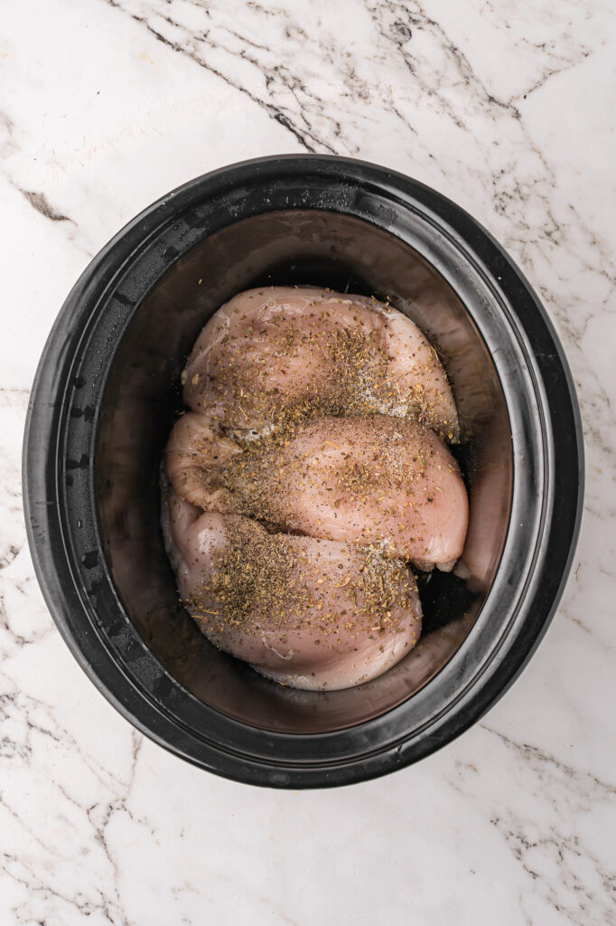 A slow cooker base with raw, seasoned chicken breasts