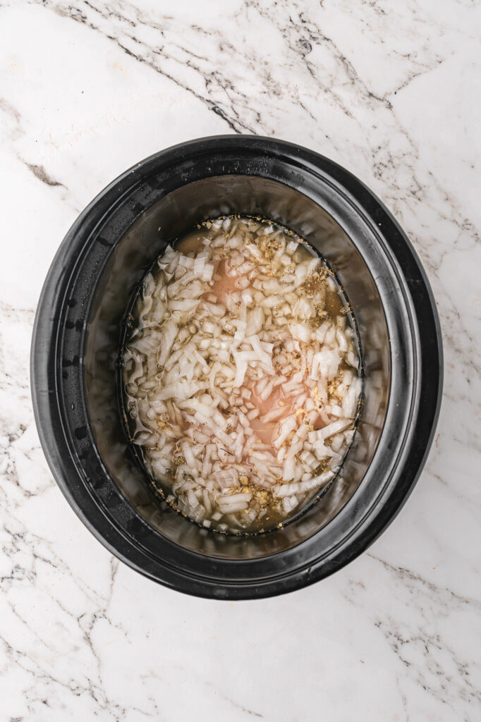A slow cooker base with raw, seasoned chicken breasts and broth
