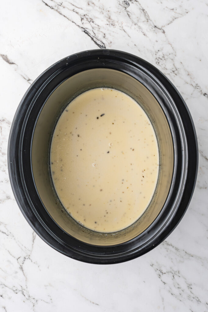 A slow cooker base with the mixed ingredients for Alfredo sauce