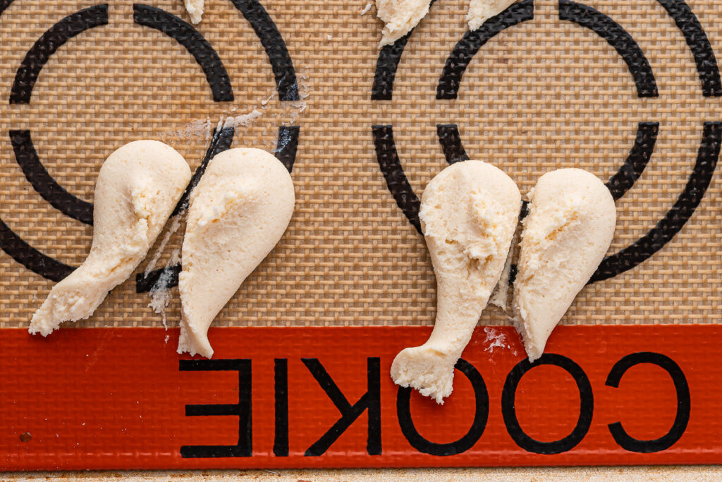 The heart-shaped cookie dough shapes split in half to create ghostly cookie dough shapes on a silicone baking mat.