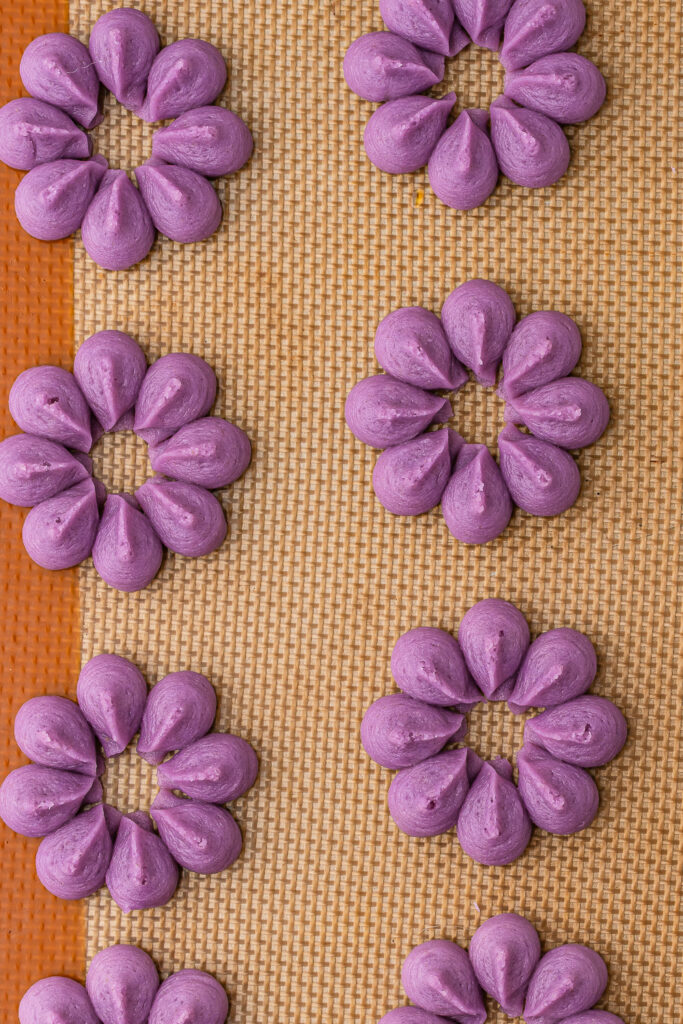Purple wreath cookie dough shapes on a silicone baking mat.