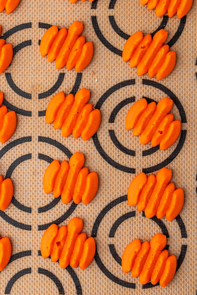 Pumpkin-shaped orange cookie dough shapes on a silicone baking mat.