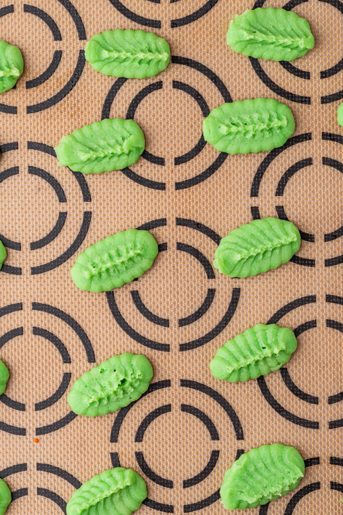 Green leaf-shaped cookie dough shapes on a silicone baking mat.